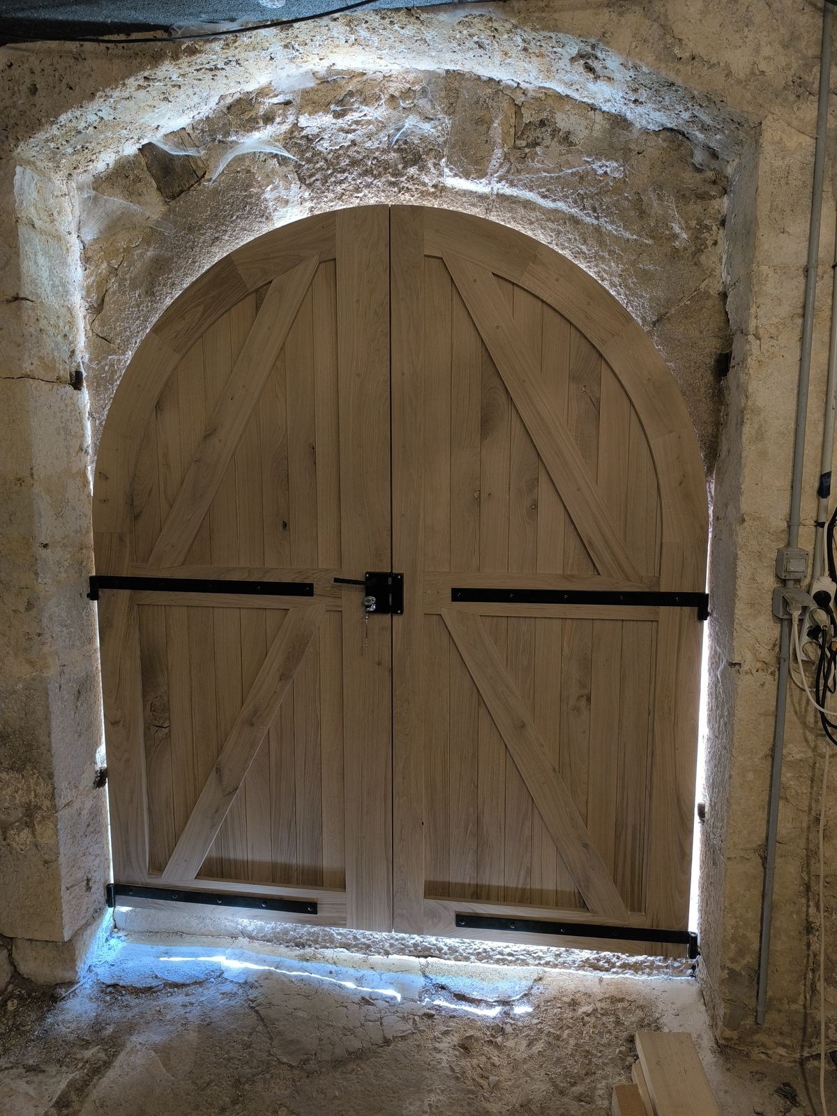 Porte de grange cintrée en chêne massif avec ferrures noires, posée dans un encadrement en pierre